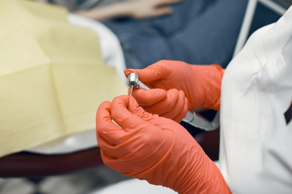orange gloves on hands of dentist holding dental syringe